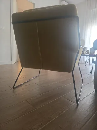 Comoda butaca mostaza con patas metálicas.