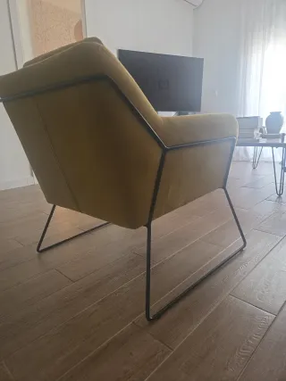 Comoda butaca mostaza con patas metálicas.