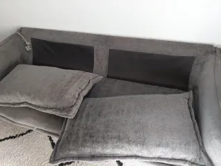 Sofá gris de tela y cojines rellenos de plumas