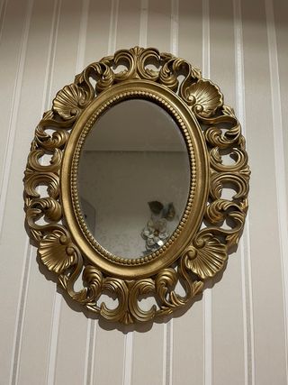 Espejo Ovalado Dorado con marco ornamentado.