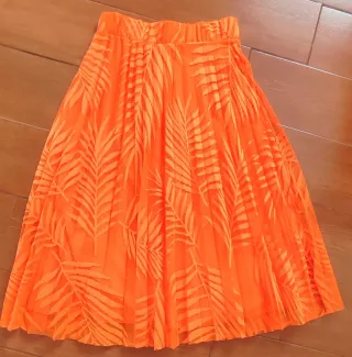 Falda naranja plisada con estampado de hojas.