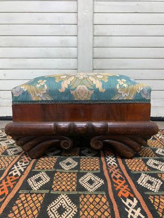 Puf baúl tapizado y con patas de madera.