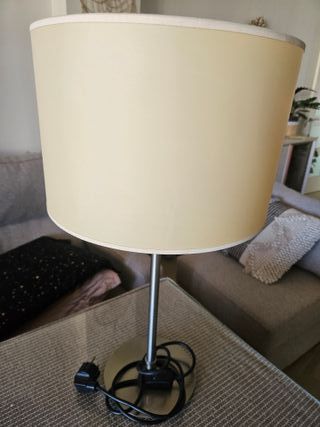 Lámpara de mesita beige/plata con pantalla rota.