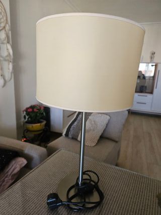 Lámpara de mesita beige/plata con pantalla rota.