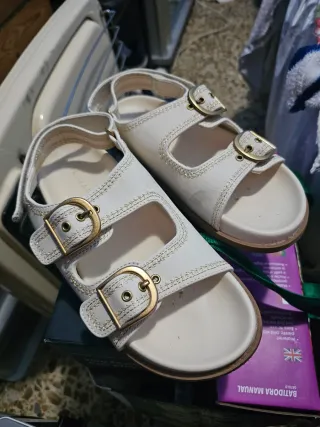 Sandalias blancas con hebillas doradas.