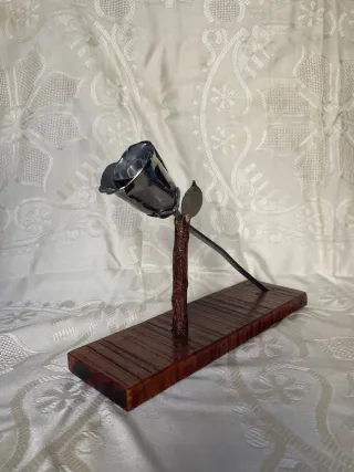 Escultura de rosa de metal, con base de madera.