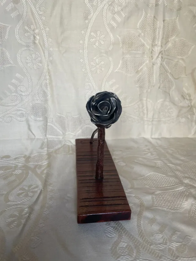 Escultura de rosa de metal, con base de madera.