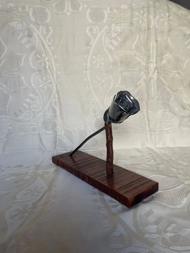 Escultura de rosa de metal, con base de madera.