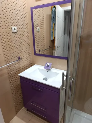 Mueble de baño morado con lavabo, espejo y grifo.