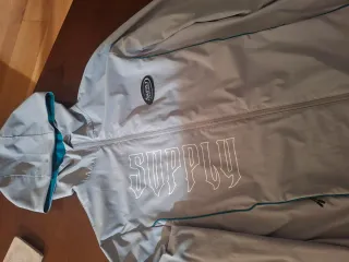 Cortavientos JD Sports Gris y Turquesa.