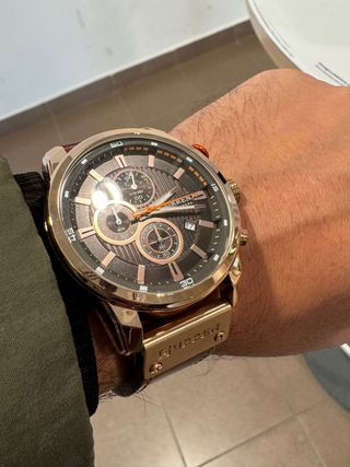 Reloj dorado–cobre con correa marrón, elegante y m