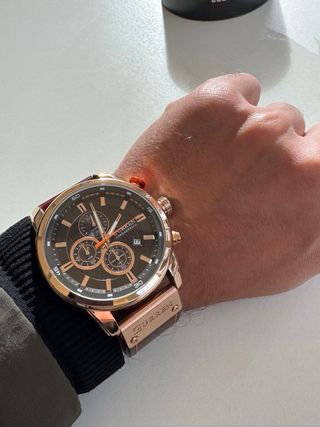 Reloj dorado–cobre con correa marrón, elegante y m