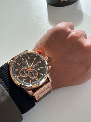 Reloj dorado–cobre con correa marrón, elegante y m