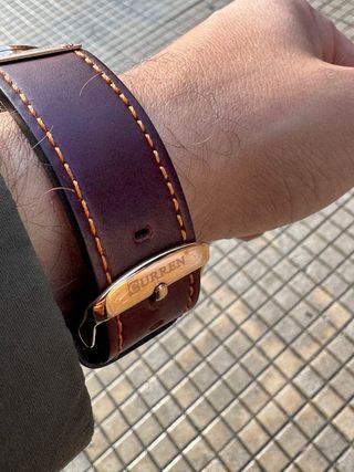 Reloj dorado–cobre con correa marrón, elegante y m