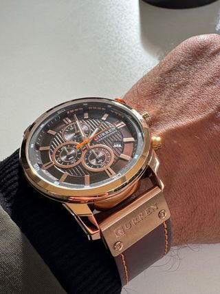 Reloj dorado–cobre con correa marrón, elegante y m