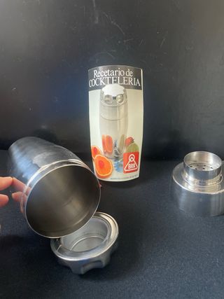 Coctelera de metal plateado con recetario.