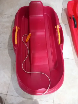 Trineo rojo con cuerda y asas de frenado.