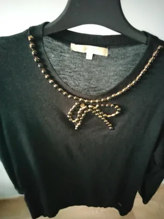 Blusa negra con detalles dorados y joya