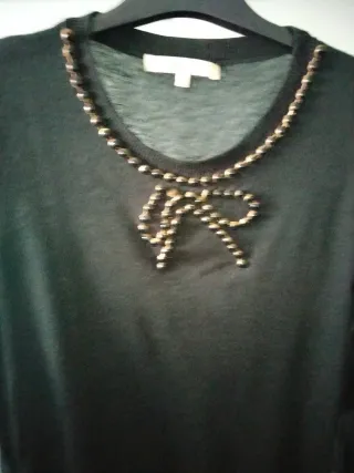 Blusa negra con detalles dorados y joya