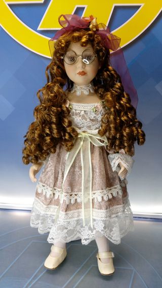 Muñeca de porcelana con gafas y vestido con encajes.