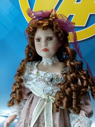 Muñeca de porcelana con gafas y vestido con encajes.