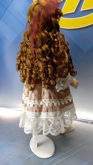 Muñeca de porcelana con gafas y vestido con encajes.