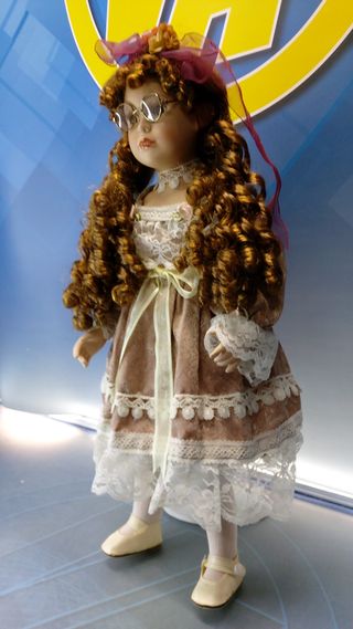 Muñeca de porcelana con gafas y vestido con encajes.