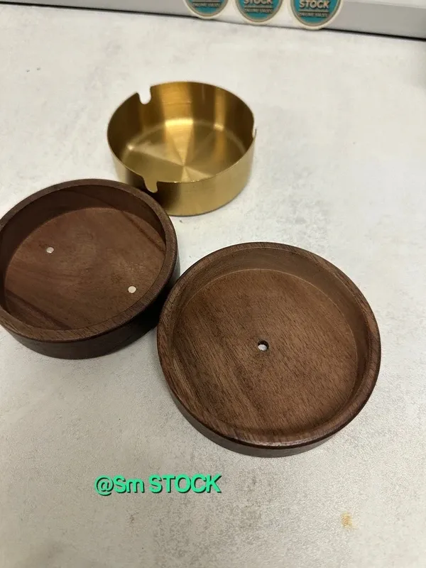 Cenicero de madera de nogal con un diseño elegante y un toque decorativo. Incluye una tapa y un pequeño adorno. - Material: Madera de nogal y metal. - Color: Marrón oscuro y dorado. - Diseño: Cil...