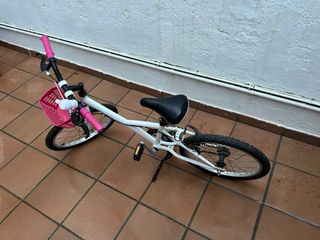 Bicicleta infantil blanca y rosa, con caballete.