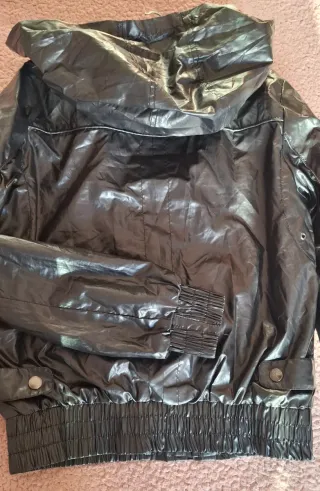 Chaqueta negra con capucha, tipo chubasquero.