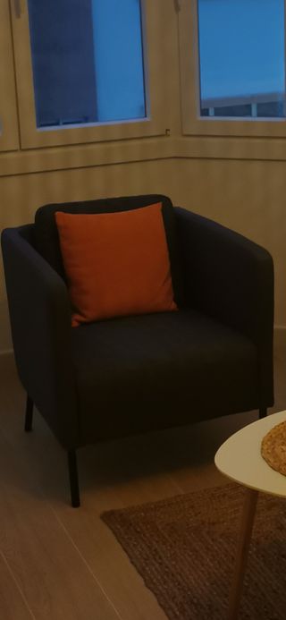 Sillón de tela gris con cojín naranja