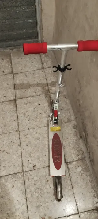 Patinete plegable plateado con ruedas rojas