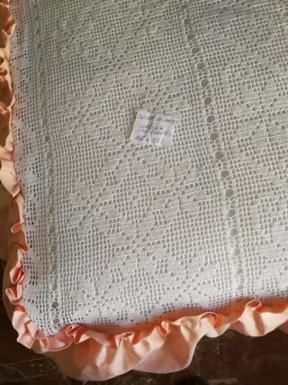 Colcha blanca d ganchillo con volante d tela rosa.