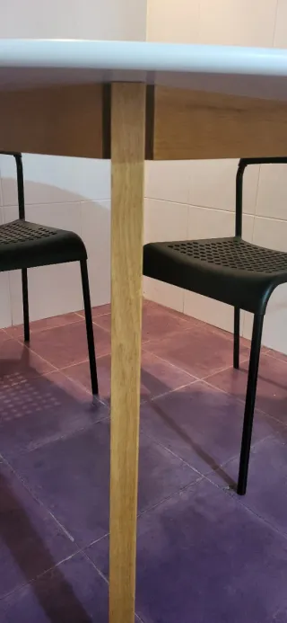 Mesa redonda blanca con 4 sillas negras de plástic