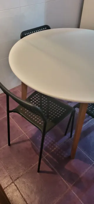 Mesa redonda blanca con 4 sillas negras de plástic