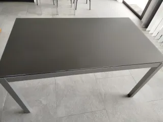 Mesa de comedor gris metálica y tapa de cristal.