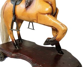 Antiguo caballo de madera sobre plataforma con ruedas de hierro.