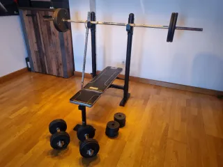 Banco de pesas con barras, discos y mancuernas.
