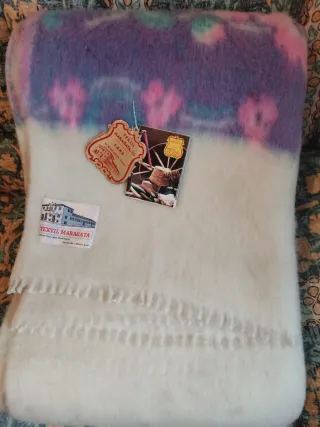 Manta de lana beige con flores moradas.