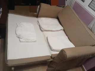 Sofá cama beige de tela y fundas blancas incluidas