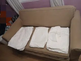 Sofá cama beige de tela y fundas blancas incluidas