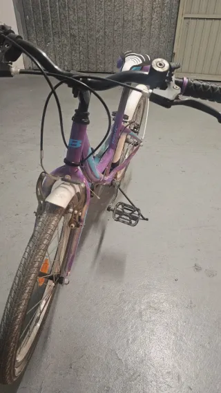 Bicicleta niña morada, tiene cesta blanca.