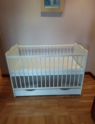 Cuna blanca con colchón y almacenamiento abajo.