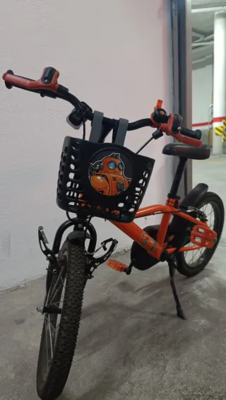Bicicleta infantil naranja con cesta y ruedines.