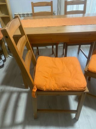 Mesa y cuatro sillas, con cojines naranjas camino