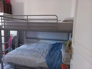 Cama alta de matrimonio de metal gris.