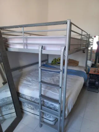 Cama alta de matrimonio de metal gris.