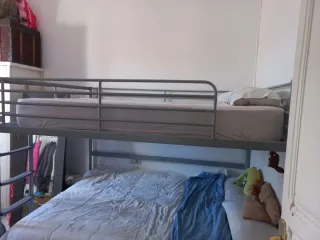 Cama alta de matrimonio de metal gris.