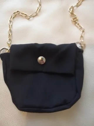 Bolso pequeño negro con cadena dorada.