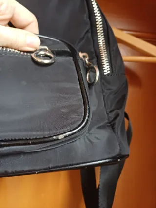 Mochila negra con varios bolsillos. Tiene rozadura